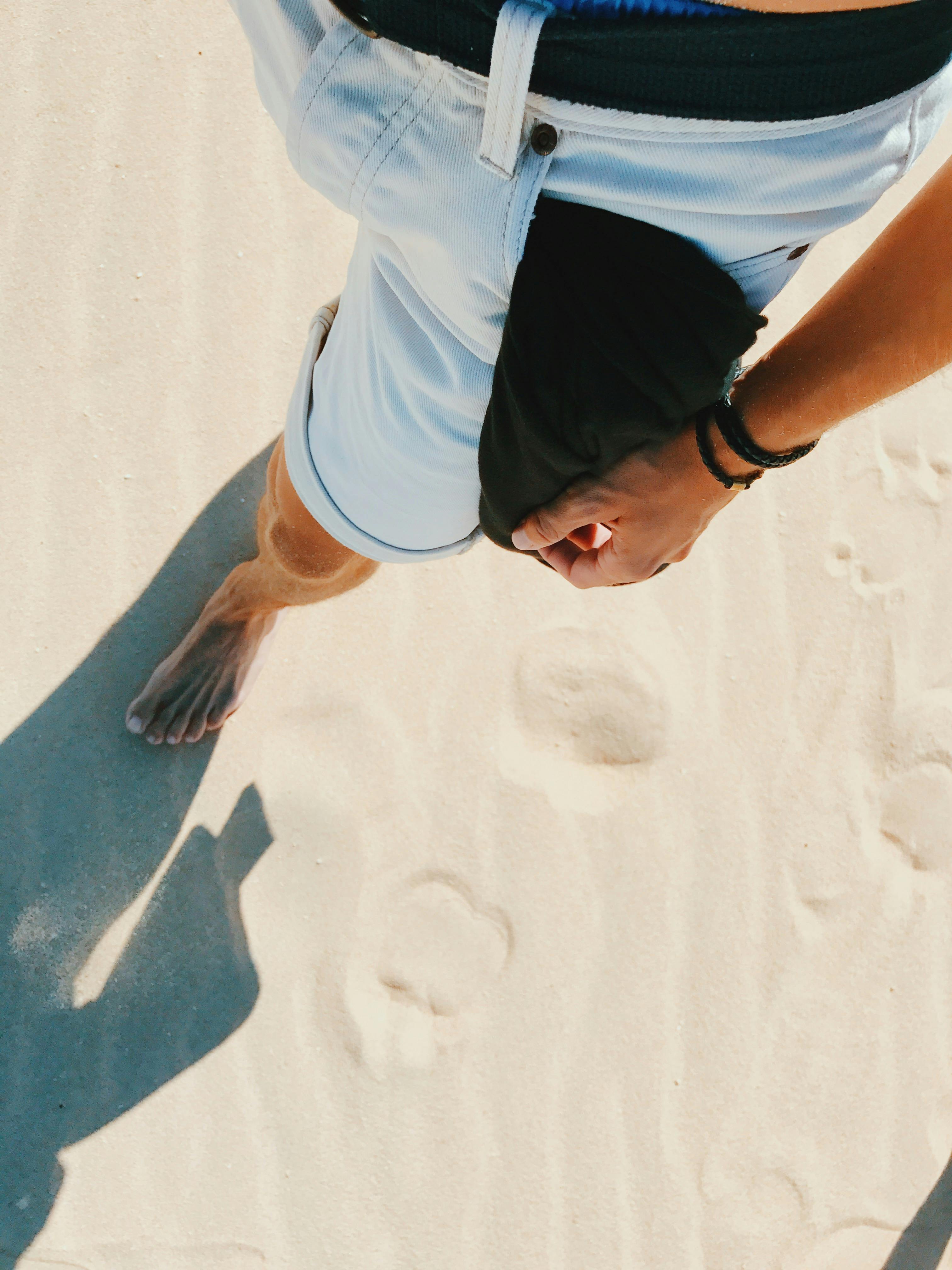 A man walks barefoot on a sandy beach, captured in La Oliva, Spain, from above.