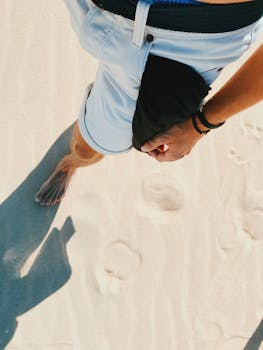 A man walks barefoot on a sandy beach, captured in La Oliva, Spain, from above.