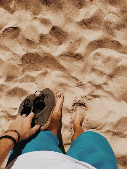 Man's legs on sunlit sand with shoes in hand at La Oliva beach.