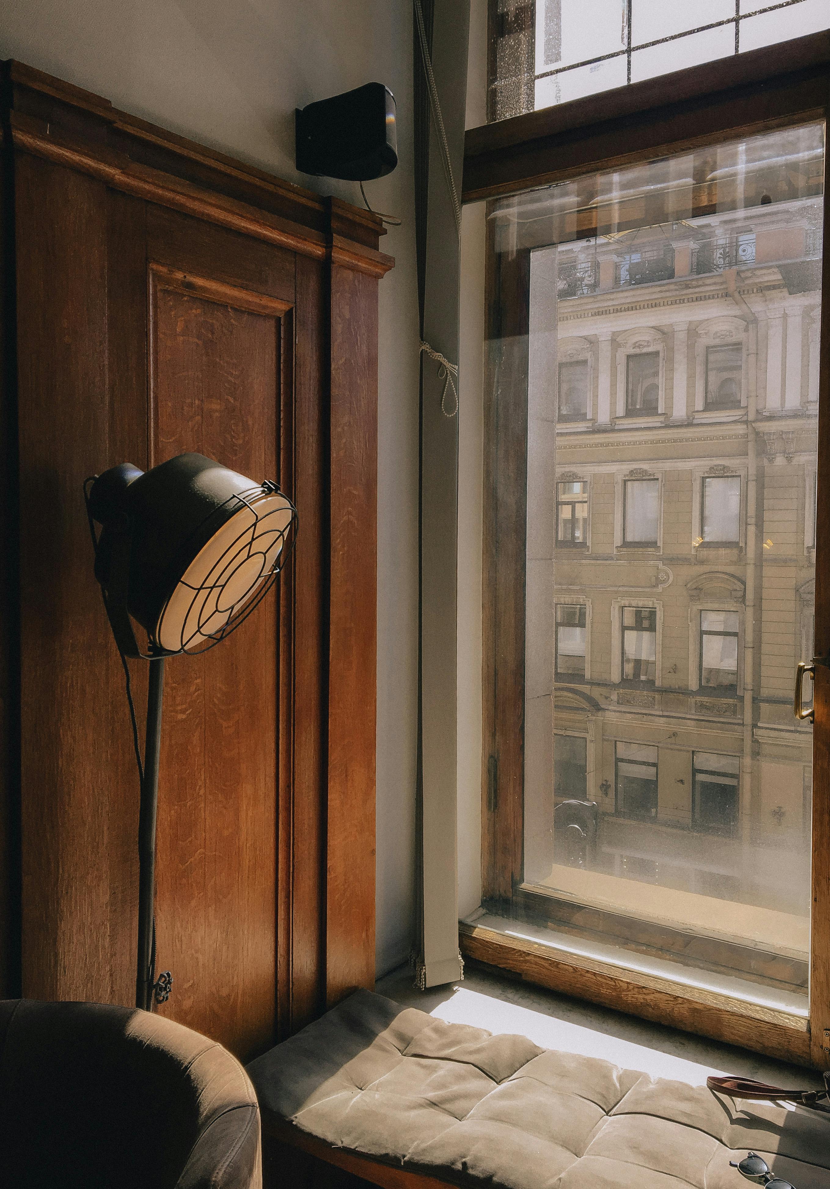 Free Sophisticated room with natural light streaming through a large window, accented by classic wooden paneling and a modern lamp. Stock Photo