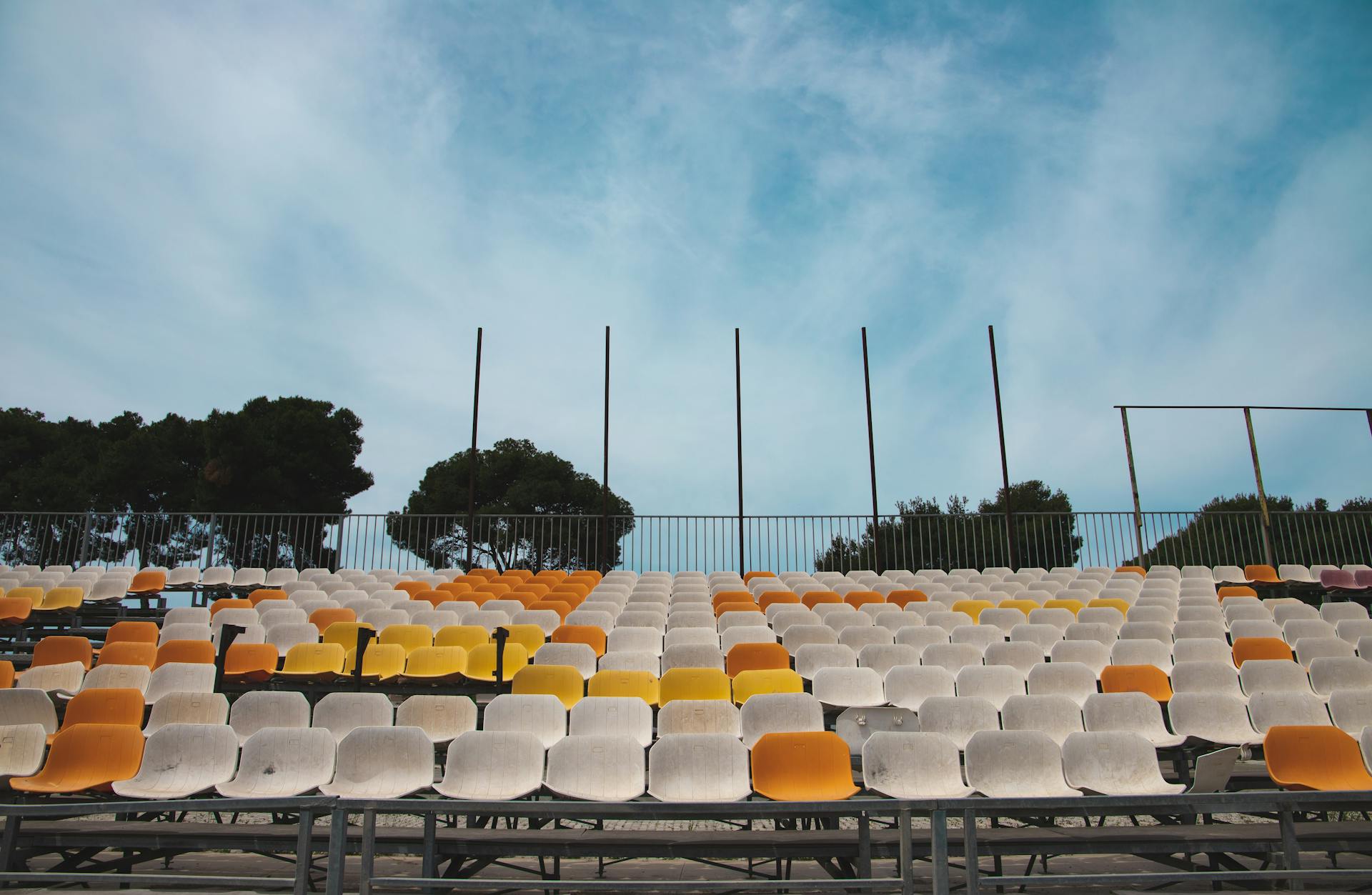 Rows of colorful empty stadium seats under a clear blue sky, providing ample copyspace.