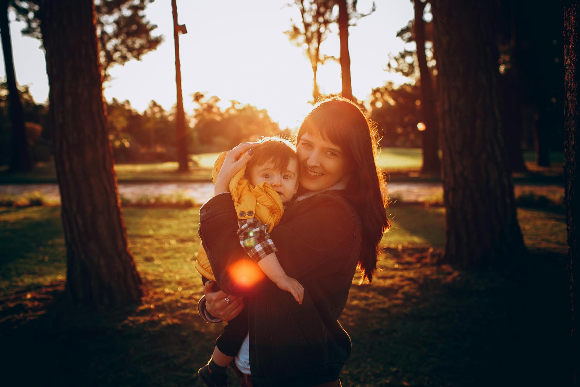 A mother joyfully embraces her child against a beautiful autumn forest backdrop, capturing a warm family moment.