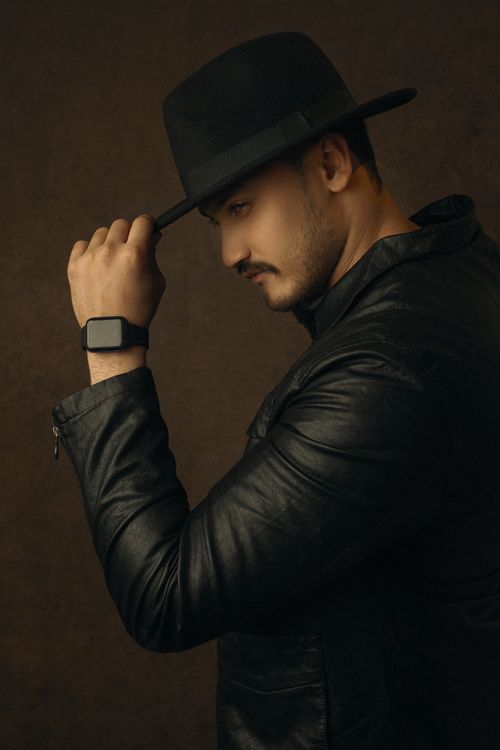 Free Portrait of a man in a leather jacket and fedora hat with warm lighting, exuding style and elegance. Stock Photo
