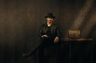 Fashionable man in black attire with fedora and vintage radio, exuding a moody ambience.