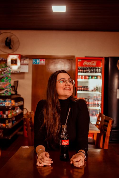 Free Woman with long hair and glasses smiling while sitting at a restaurant table with a Coke bottle. Stock Photo