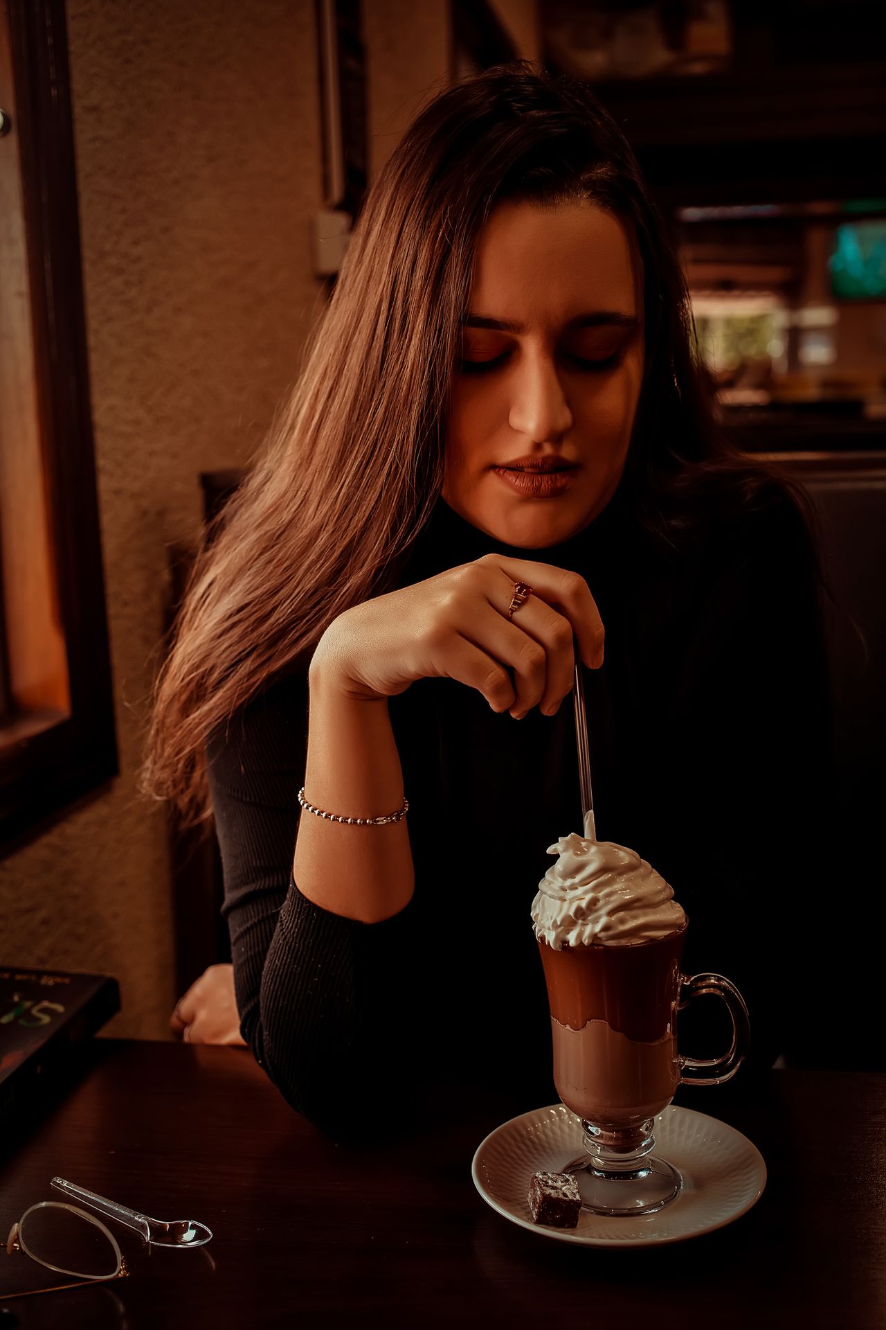Woman stirring a whipped-cream topped hot chocolate in a cafe