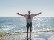 年长的男人张开双臂享受海滩，在阳光明媚的天空下散发着自由和欢乐