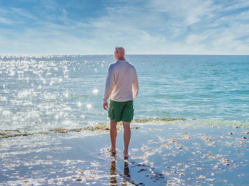 Man in White Shirt and Green Shorts Standing on Seashore