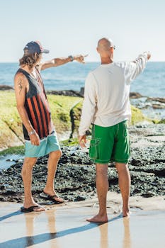 Two friends on a beach pointing towards the sea, expressing casual lifestyle and summer vibes.