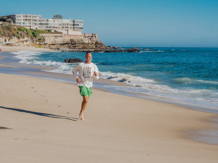 A Man In White Sweatshirt Running On The Beach Sand