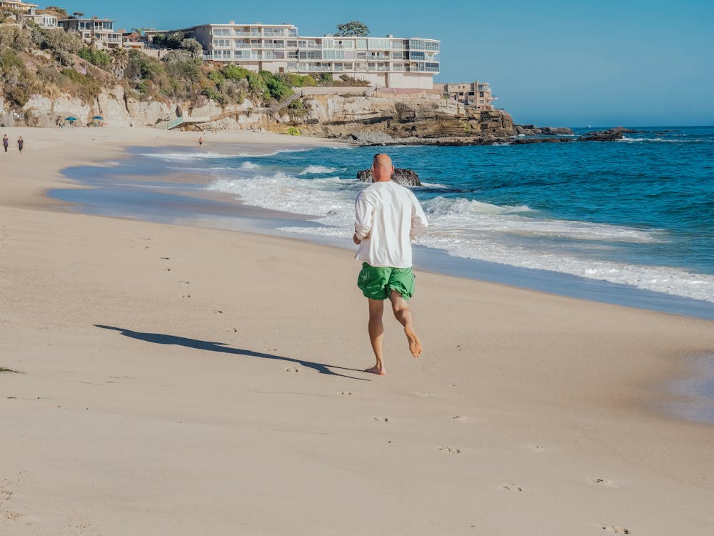 Man in White Shirt and Green Shorts Walking on Beach