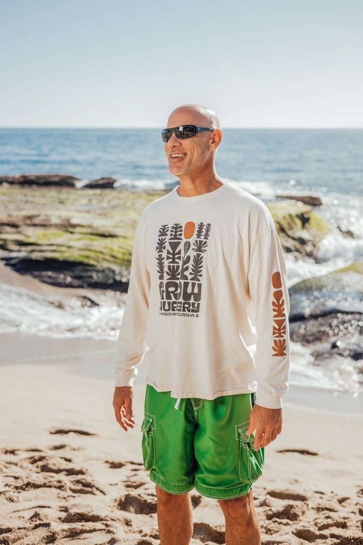 An Elderly Man In White Sweatshirt Smiling While Standing On The Beach