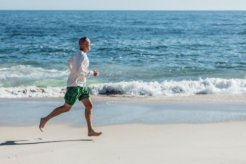 Free Man in White Shirt and Green Shorts Running on Beach Stock Photo