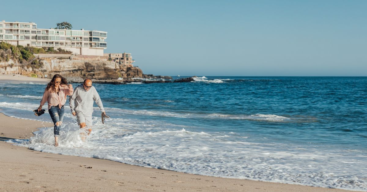 Senior couple splashing in ocean waves during a summer beach walk, capturing joyful vacation moments.