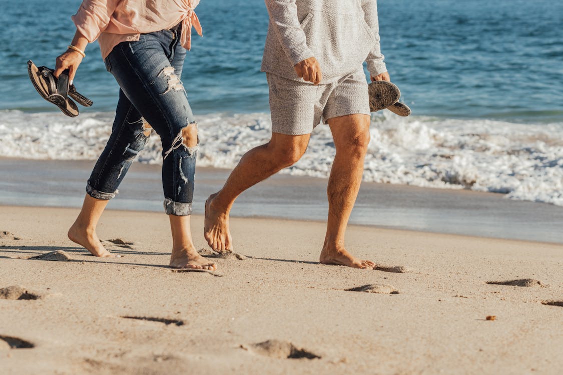Free Person in White Shirt and Blue Denim Jeans Walking on Beach Stock Photo