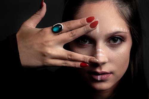 Serious female with dark hair and creating makeup making Vulcan salute gesture and looking at camera against black background