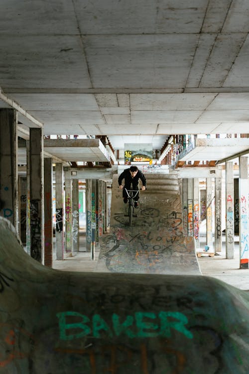 Man in Black Jacket Riding a Bicycle on Skate Ramp in an Abandoned Building