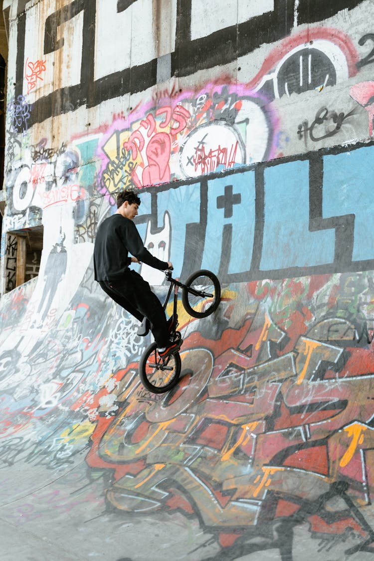 Young Man In Black Long Sleeve Shirt Riding A Bicycle Doing Trick Work On Skate Ramp