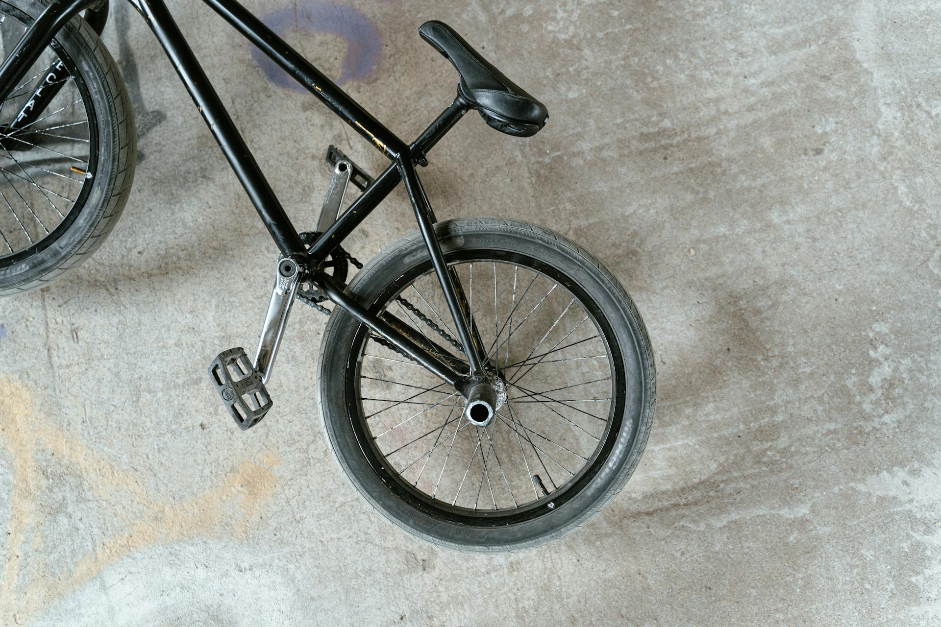 Black BMX bike viewed from above on a concrete surface, showcasing rear wheel and frame details.