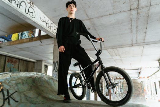 A BMX biker in black clothing poses confidently with a bike against a graffiti backdrop.