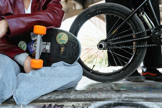 A person sitting with a skateboard and BMX bike, showcasing urban street lifestyle.