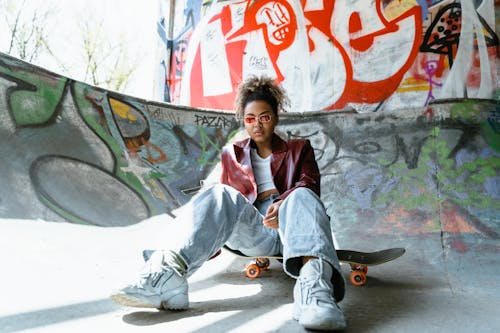 Woman in Red Coat and Denim Pants Sitting on Skateboard 