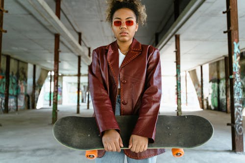 Young Woman Standing in Red Leather Jacket Holding a Skateboard 