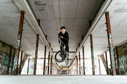 A BMX rider performs a trick mid-air in an abandoned building covered in graffiti.. rider, performs, trick