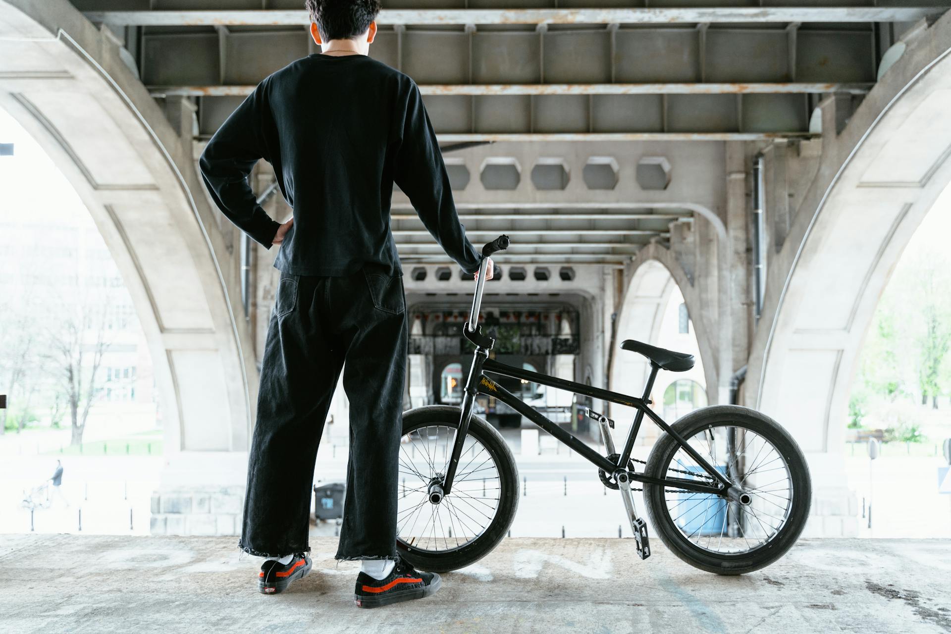A young male BMX rider stands with his bike under an urban bridge, showcasing urban lifestyle.