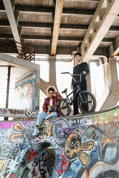 Free Two young adults explore a graffiti-filled skate park with a BMX bike under an urban bridge. Stock Photo