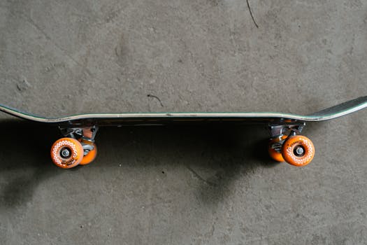 Close-up of a skateboard with orange wheels on a concrete floor.