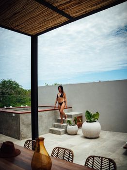 Woman in black bikini enjoying a sunny day at a modern villa poolside.