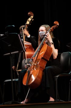 Female cellist playing during an indoor music concert, wearing a mask.