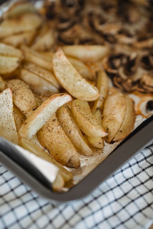 Free Crispy golden potato wedges baked to perfection on a tray with seasonings. Stock Photo