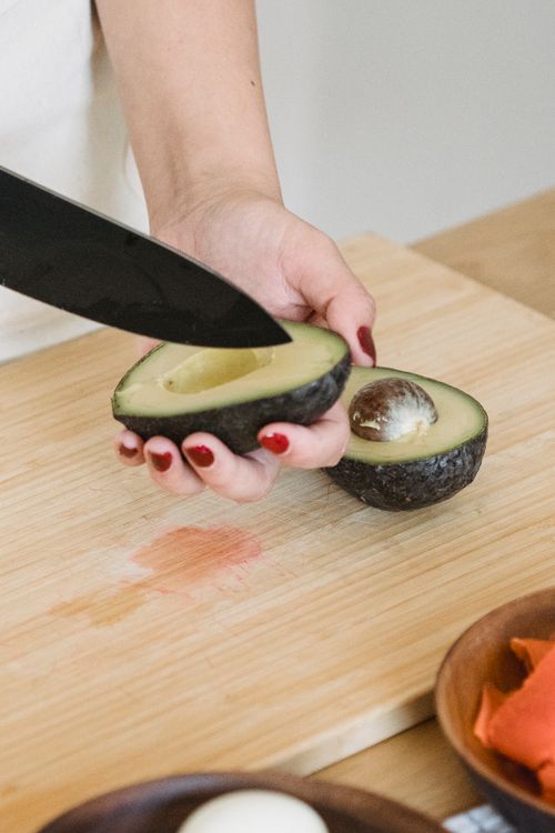 Free A woman cutting an avocado in a kitchen setting, highlighting healthy cooking preparation. Stock Photo