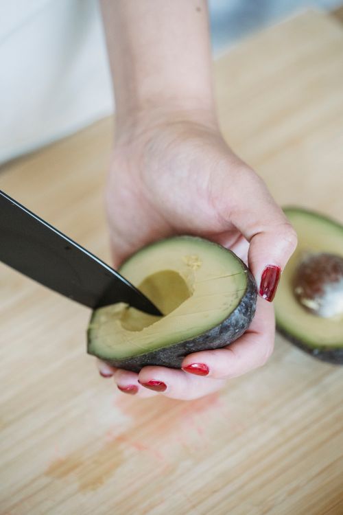 Free Close-up of a hand slicing an avocado on a wooden board with a knife. Stock Photo