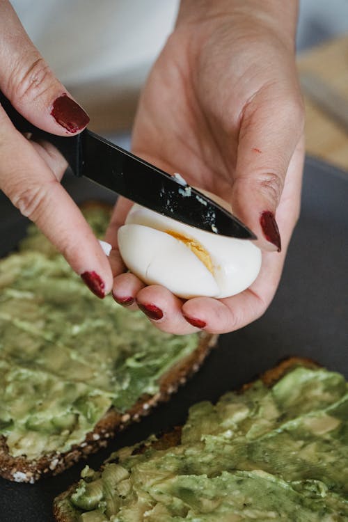 Free Hands of a Person Slicing a Boiled Egg Over Avocado Toast Stock Photo