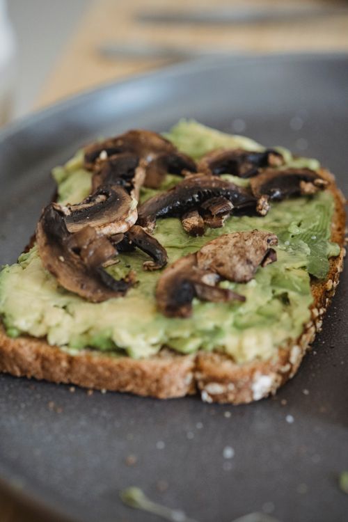 Free Delicious avocado toast topped with sautéed mushrooms on a dark plate, perfect for breakfast or brunch. Stock Photo