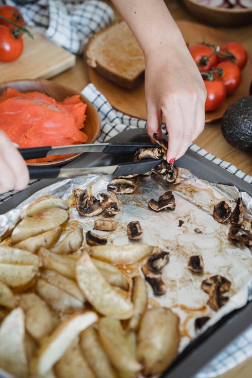 Free Close-up of hands arranging roasted mushrooms and potatoes on a baking tray, surrounded by fresh vegetables. Stock Photo