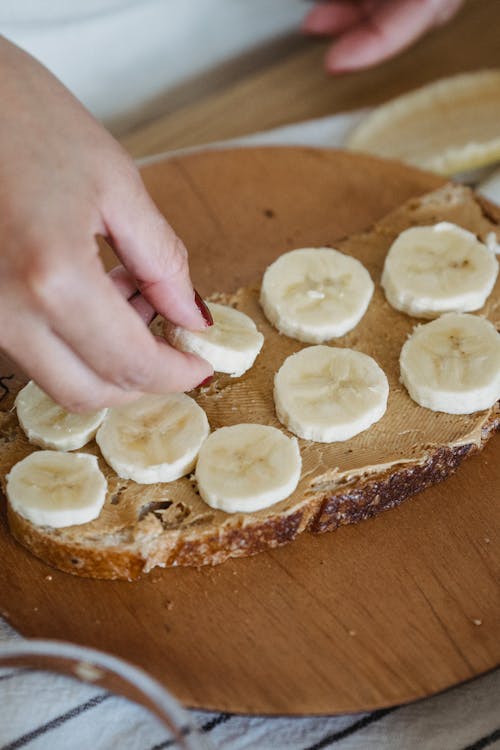 Person Arranging Slices of Banana on a Bread