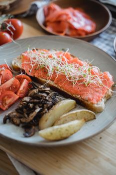 Close-up of a salmon open sandwich with vegetables and mushrooms on a ceramic plate.