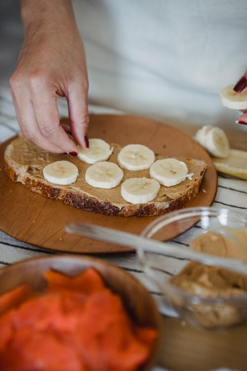 Free Hand of a Person Preparing Banana and Peanut Butter Toast Stock Photo