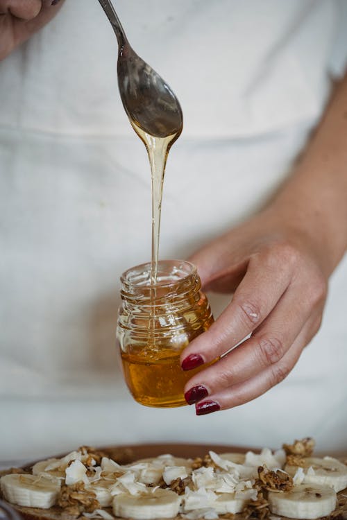 Person Holding a Spoon and a Glass Jar of Honey