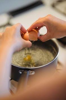 A person cracks an egg into a pot of boiling water, preparing a poached egg.