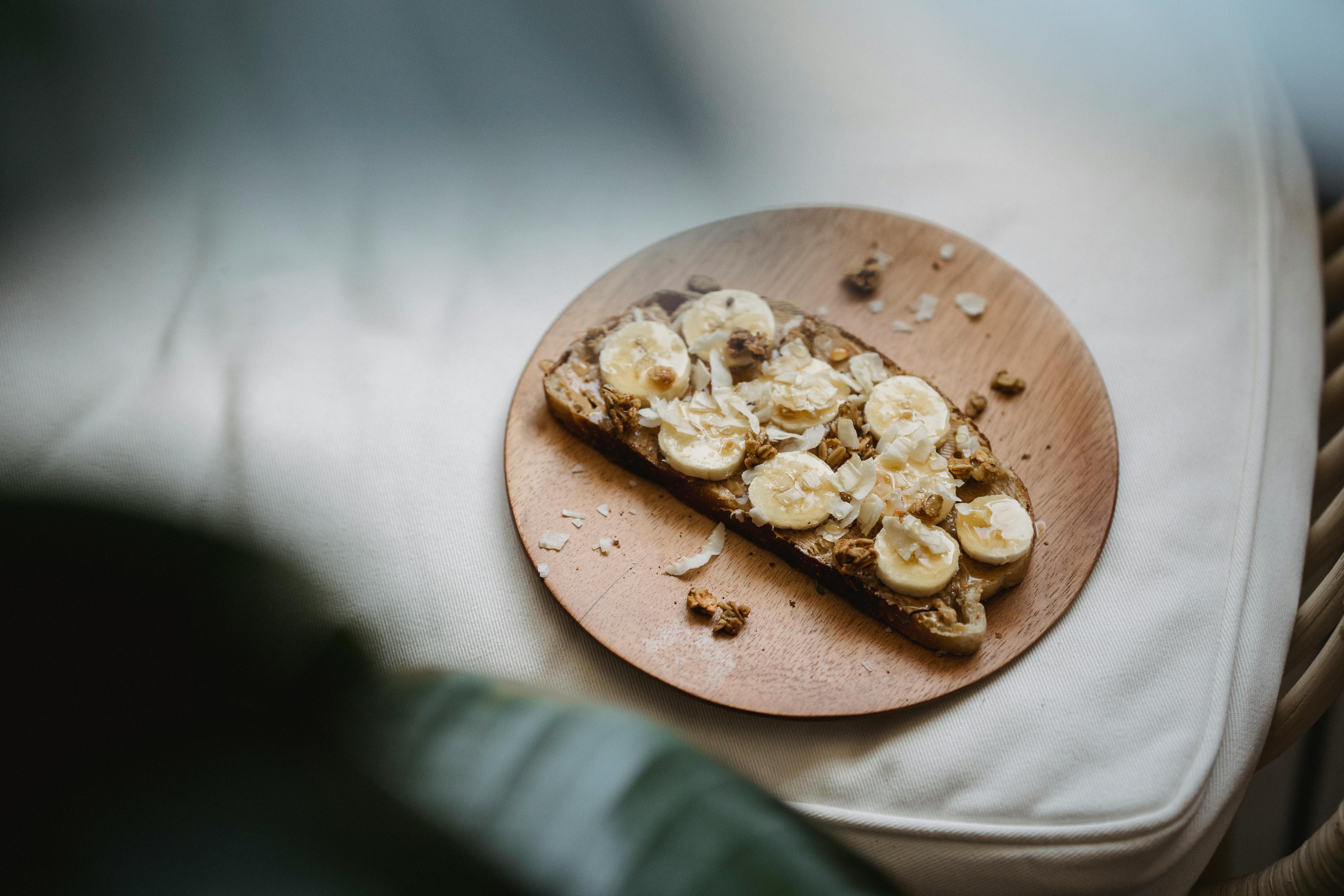 Sliced banana and peanut butter on rye toast presented on a wooden plate, offering a healthy snack.