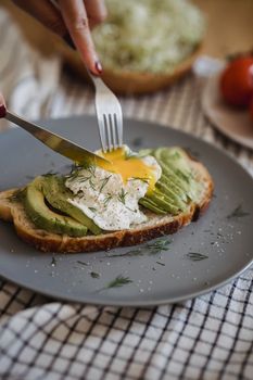 A close-up of avocado toast topped with egg, garnished with herbs on a grey plate.