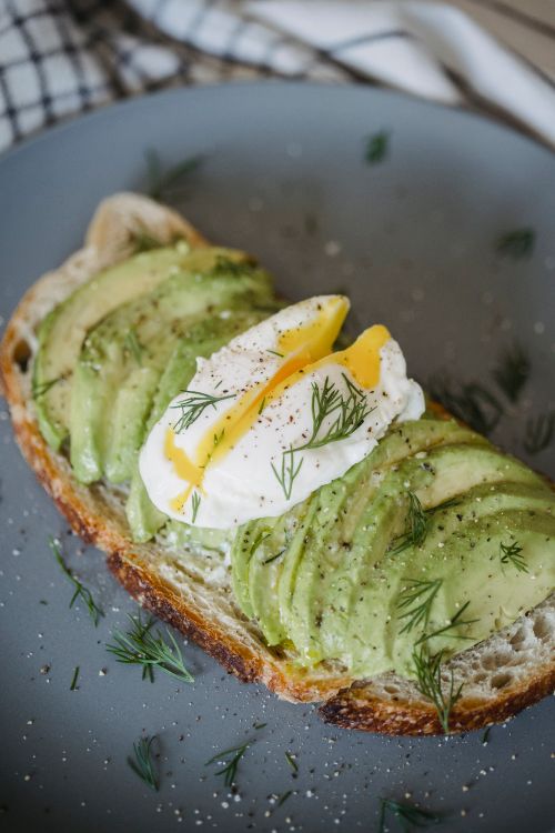 Free Mouthwatering avocado toast topped with a poached egg, perfect for a healthy breakfast. Stock Photo