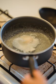 A fresh poached egg boiling in a pot on a gas stove, captured in close-up detail.
