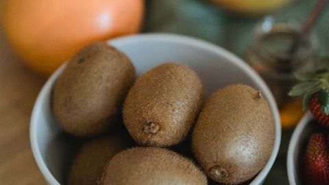 Close-up of fresh kiwi and citrus fruits in white bowls on a wooden table. Perfect for healthy eating themes.