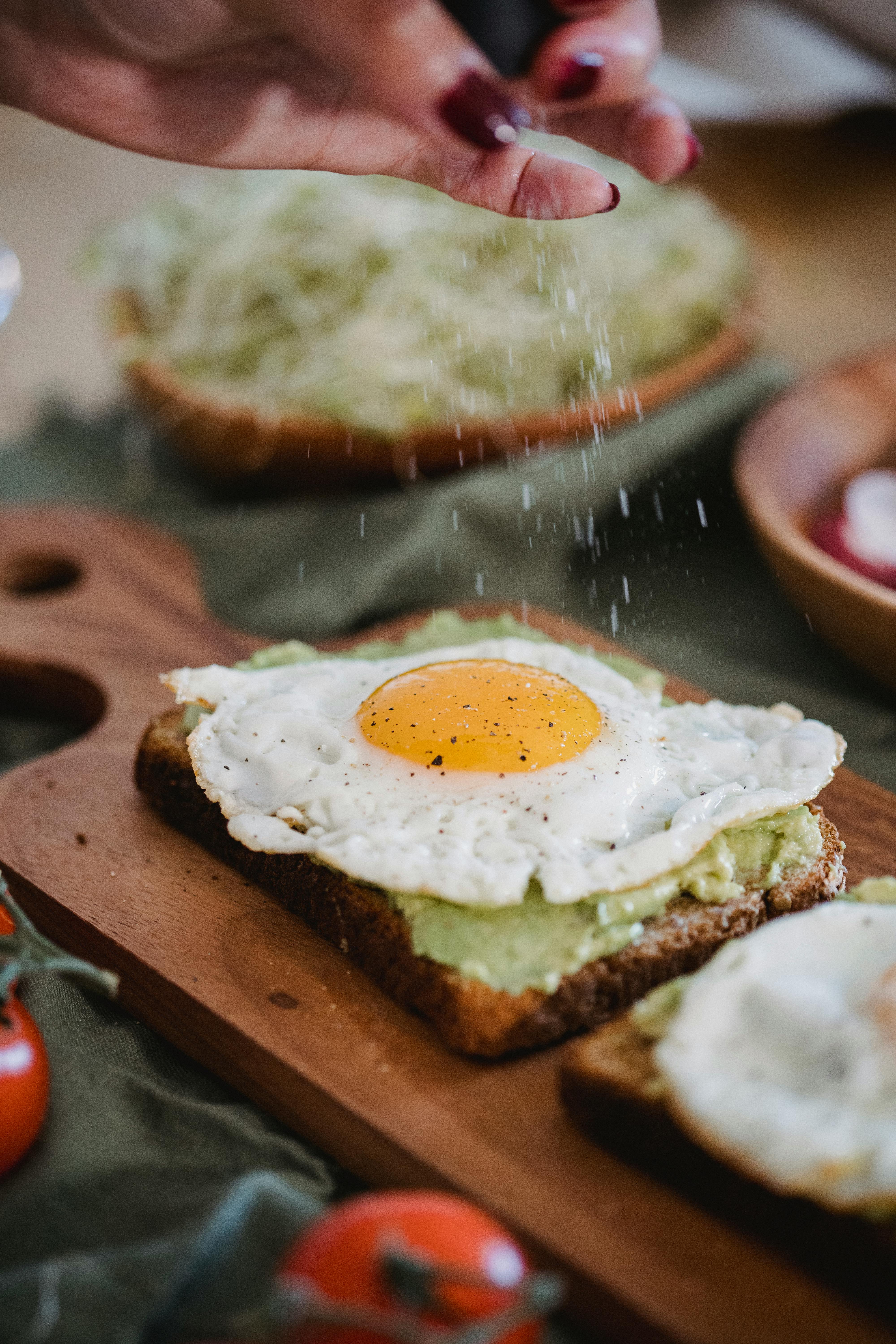Close-up of avocado toast topped with a fried egg, garnished with salt, perfect for breakfast.